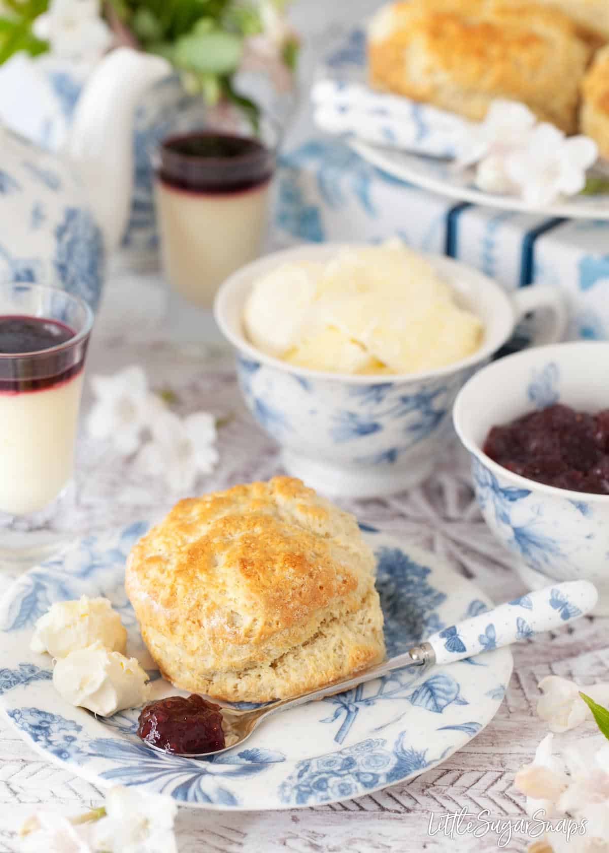 An English scone with 2 scoops of clotted cream and a spoon with raspberry jam.